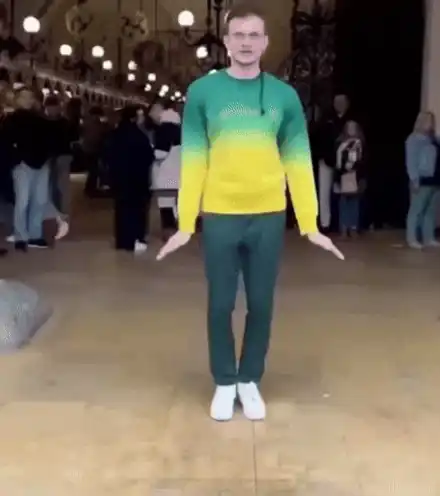 Vitalik Buterin walking with arms out, wearing a green-to-yellow gradient sweater